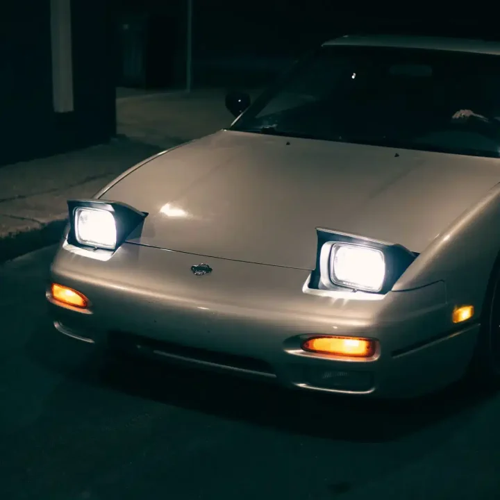 A classic car with pop-up headlights illuminated on a street at night.